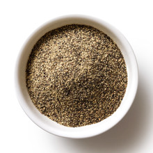 Finely ground black pepper in white ceramic bowl isolated on white from above.