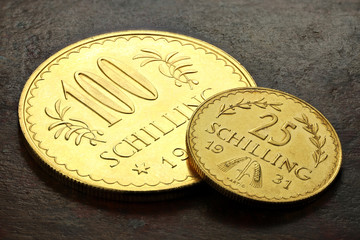 Austrian 25 and 100 Schilling gold coins on rustic wooden background