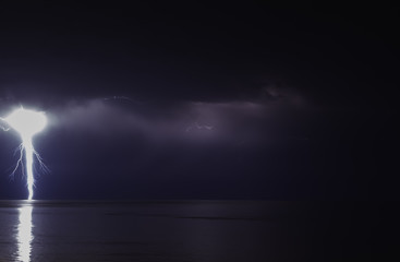 Wall Mural - lightning bolts reflection over the sea. taken during a thunderstorm over the ocean with clouds in the background