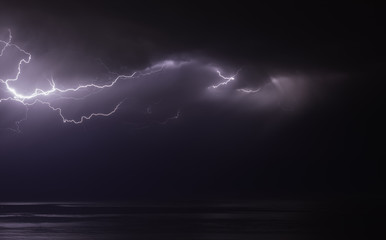 Wall Mural - lightning bolts reflection over the sea. taken during a thunderstorm over the ocean with clouds in the background