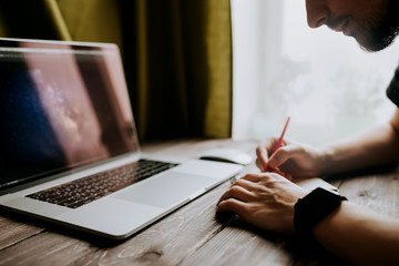 Fototapete - Man is writing on draft notepad and using laptop computer and at home office. Freelance lifestyle workplace
