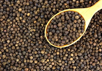 Wall Mural - Black peppercorn seeds background with a wooden spoon