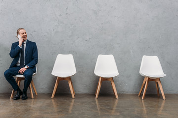 Wall Mural - young handsome businessman talking by phone while sitting on chair