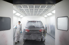 Auto Painter Painting A Car Inside A Paint Booth