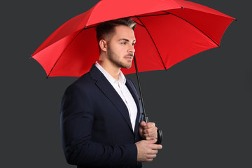 Poster - Young man in elegant suit with red umbrella on dark background