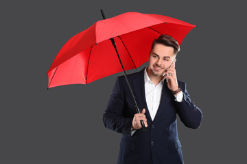 Canvas Print - Young man with red umbrella talking on cell phone against dark background