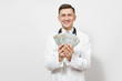 © ViDi Studio - Smiling young doctor man isolated on white background. Male doctor in medical uniform, stethoscope holding bundle of dollars, banknotes, cash money. Healthcare personnel, health, medicine concept.