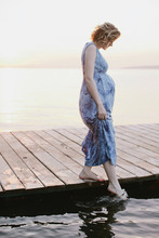 Side View Portrait Of Young Pregnant Woman Standing On Deck And Touching The Water With Feet