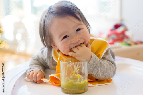 Fototapeta Happy little baby boy eating food in his house