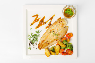 Grilled fish fillets steak served with mix vegetable, potatoes and a glass of black pepper gravy sauce on white background