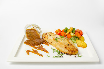 Wall Mural - Grilled fish fillets steak served with mix vegetable, potatoes and a glass of black pepper gravy sauce on white background