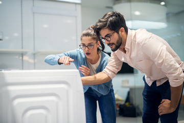 Wall Mural - Young amazed love couple standing in the front of new electronic product and testing operation in the tech store.