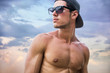 © theartofphoto - Attractive shirtless athletic young man on beach by the sea, with baseball cap and sunglasses, looking away