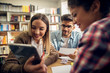 © Dusan Petkovic - Close up of three smiling lovely playful young students sitting in the high school library and looking in a tablet while sitting at the desk together.
