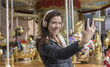 © Outsiderzone - joy, woman next to a merry-go-round taking selfie with the cell phone on a spring afternoon. image of freshness and lifestyle in europe