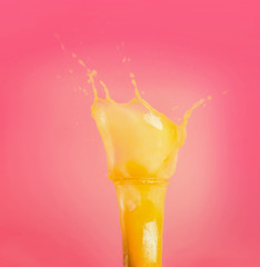 Glass with yellow splash summer beverage: smoothie or juice at pink background, front view