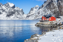 Red Fisherman´s House On Lofoten Islands In Front Of A Fjord At A Beautiful Sunny Winter Day