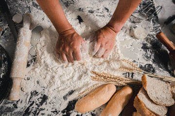 Wall Mural - Man preparing buns at table in bakery, Man sprinkling flour over fresh dough on kitchen table