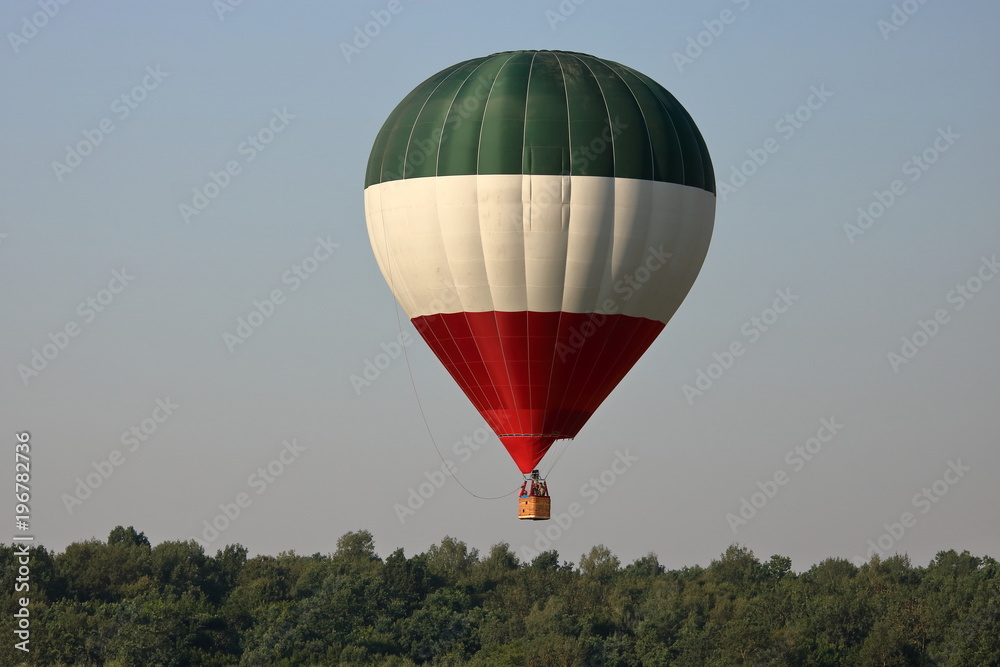 Balon na rozgrzane powietrze, w pasy zielony, biały i czerwony, w powietrzu, ponad drzewami - obrazy, fototapety, plakaty 