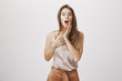 © Cookie Studio - Hearing shocking news that sweep girl from feet. Portrait of surprised and thrilled attractive woman in feminine stylish clothes, holding hands on chest and near opened mouth, gasping from amazement