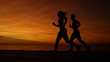 © helivideo - SILHOUETTE: Young woman and man go for an evening jog on a breathtaking evening