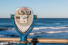 Coin-operated Binoculars On A Fishing Pier With A View Of Ocean Waves In The Distance. 