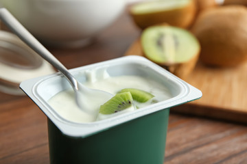 Canvas Print - Plastic cup of yummy kiwi yogurt on wooden table, closeup