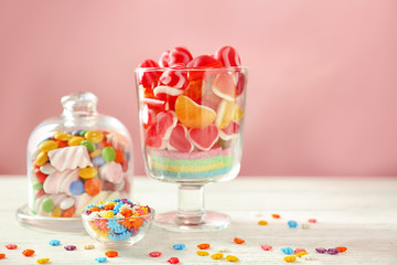 Canvas Print - Glassware with sprinkles and different candies on table against color background