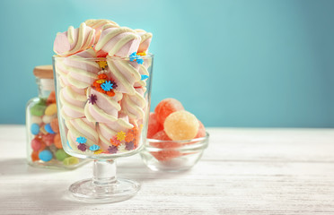 Wall Mural - Glassware with marshmallows, sprinkles and different candies on table against color background