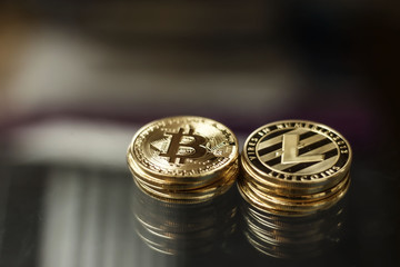 Physical version of Bitcoin and Litecoin. Golden, shining coins on a dark background.