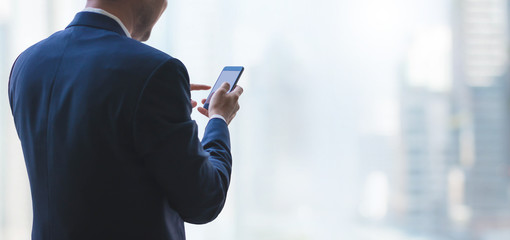 Business man using smart phone on window with city building background and copy space.Concept of business people use technology.