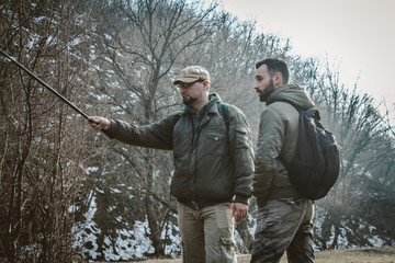 Two men talking in nature and carry backpacks and fishing rods.