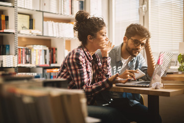 Wall Mural - Two attractive hardworking young students struggling with homework in the school library.