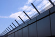 Safety wall with barbed wire and spikes on top of a fence provide security - blue sky background with copy space