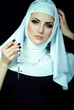 Яркий макияж на лице у девушки. Красивая монахиня с крестом. Портрет леди на черном фоне. Макияж и косметика.
