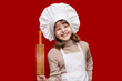 © Svetlana - Portrait of happy little girl in chef uniform holds a rolling pin isolated on red. Kid chef. Cooking Process Concept