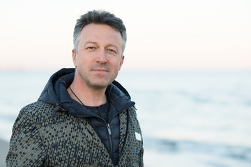 Handsome middle-aged man at the beach. Attractive happy smiling mid adult male model posing at seaside, sunset o sunrise. Outdoor portrait of beautiful man.