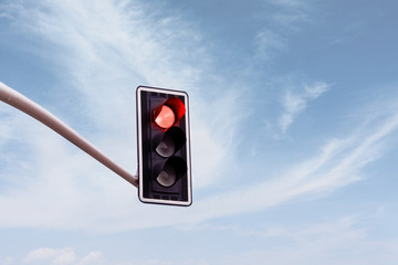 Red traffic light on a horizontal white metal beam, isolated on sky background