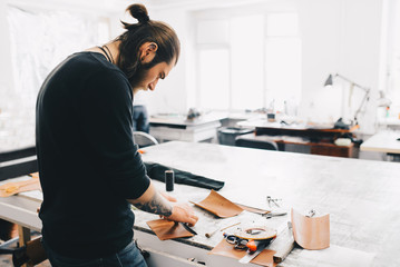 Working process of the leather bag in the leather workshop. Man holding crafting tool and working. Work table background. Free space.