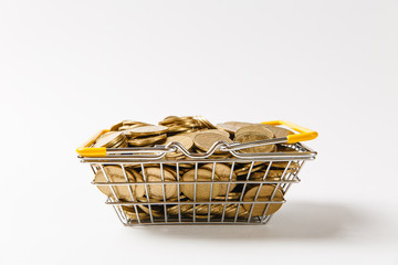 Wall Mural - Close up of metal grocery basket for shopping in supermarket with lowered yellow handles filled with golden coins isolated on white background. Concept of shopping, money. Copy space for advertisement