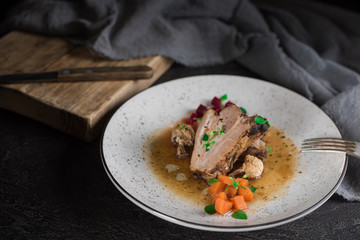 Wall Mural - Pork ribs with beets, carrots, fried mushrooms and sauce on a white plate. Restaurant serving. Old black rustic background. Top view