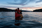 Fototapeta Do akwarium - Couple friends on a wooden canoe are paddling in an inlet surrounded by Canadian mountains during a vibrant sunset. Taken in Indian Arm, near Deep Cove, North Vancouver, British Columbia, Canada.