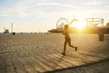 Athletic African American Woman Jogging On Boardwalk At Sunset