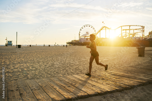 Fotografía athletic african american woman jogging on boardwalk at sunset