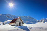 Fototapeta Krajobraz - Winter landscape with wooden toolshed and Fagaras Mountains covered in thick layer of snow at Balea lake, Sibiu county, Romania
