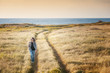 © olezzo - Beautiful seascape at sunset, young stylish woman traveler walks on lawn overlooking the sea