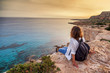 Leinwandbild Motiv A stylish young woman traveler watches a beautiful sunset on the rocks on the beach, Cyprus, Cape Greco, a popular destination for summer travel in Europe