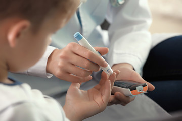 Wall Mural - Doctor using lancet pen and digital glucometer to check diabetic boy's blood sugar level, closeup