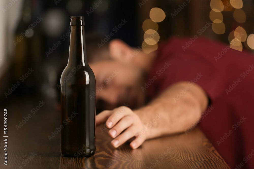 Man reaching for bottle of drink in bar. Alcoholism problem