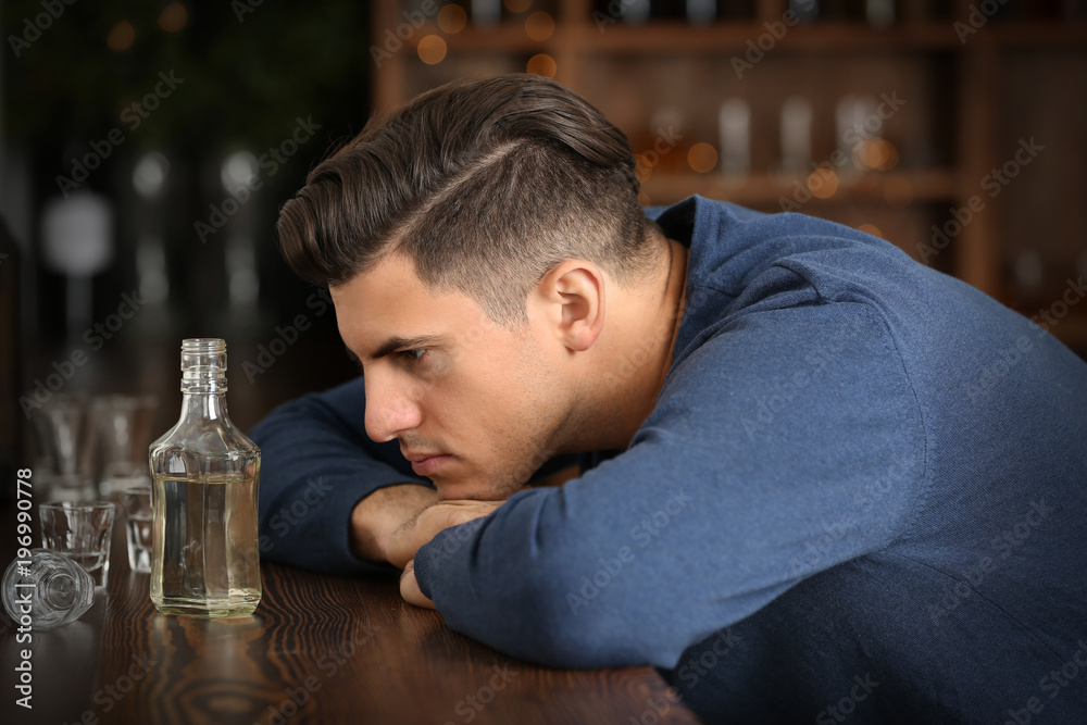 Young man with bottle of drink in bar. Alcoholism problem